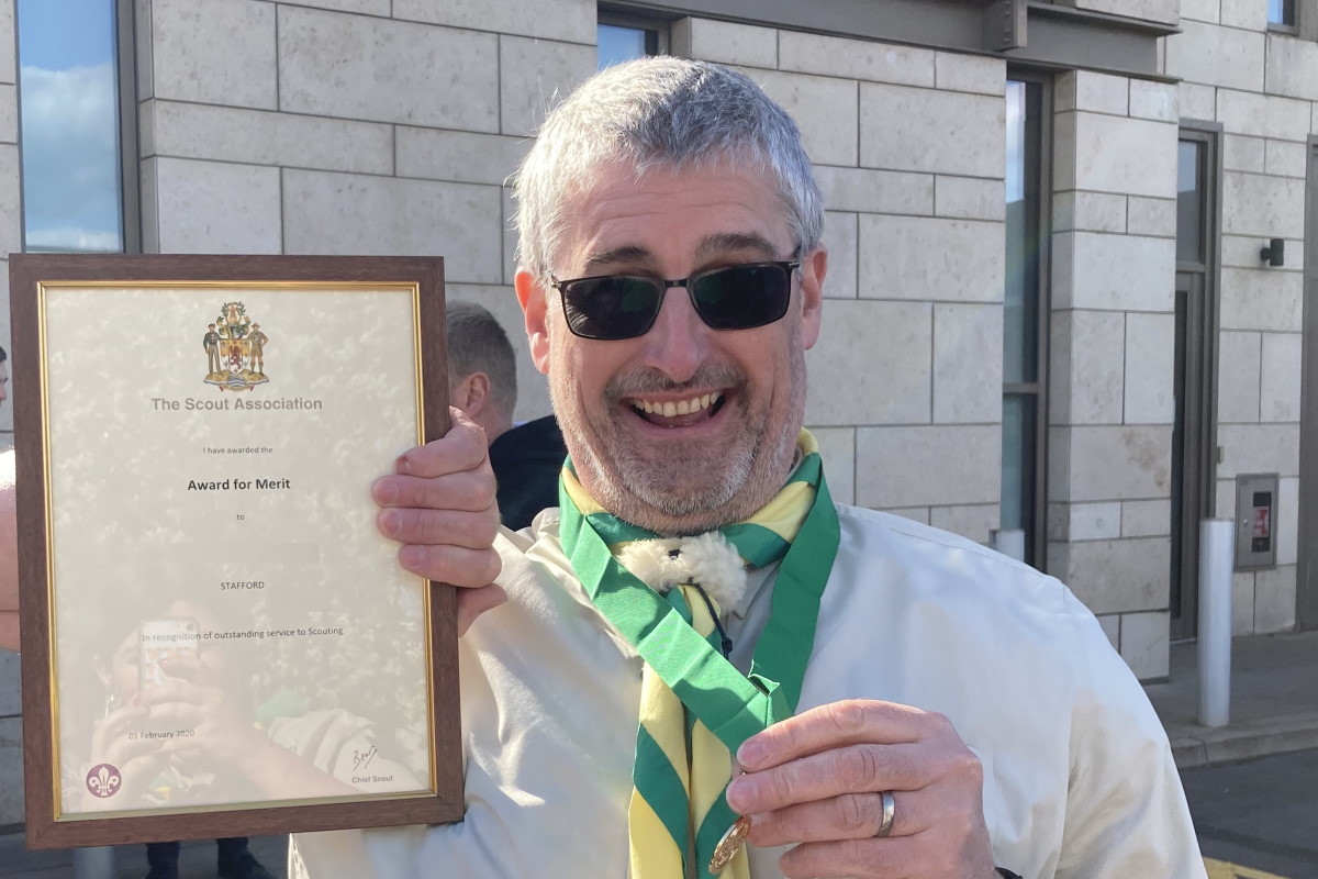 Image of a male adult volunteer holding an Award for Merit certificate